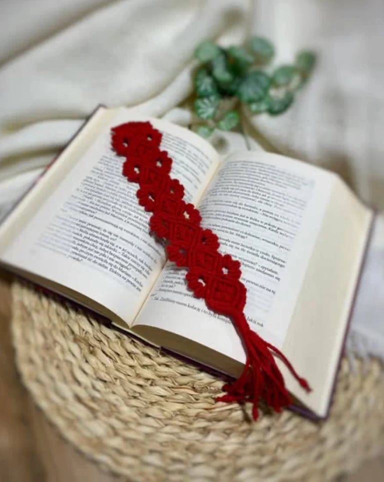 Open book with red crocheted bookmark resting on pages, placed on woven circular mat with eucalyptus sprigs in background