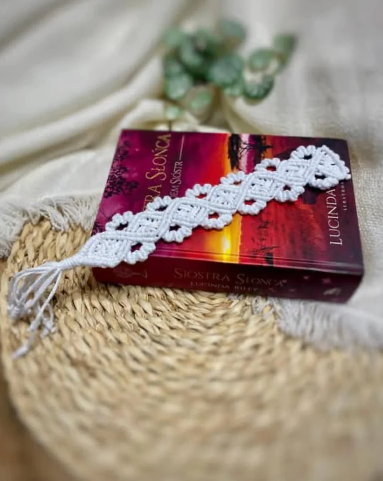 Red book with white decorative lace ribbon on woven beige fabric with dried eucalyptus in background